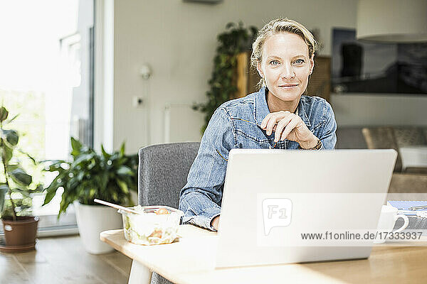 Selbstbewusste Geschäftsfrau mit Laptop,  die zu Hause sitzt