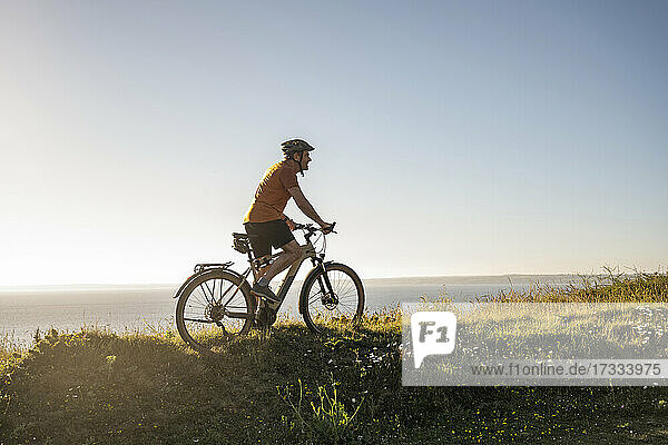 Male sportsperson riding electric mountain bike on green grass at sunset
