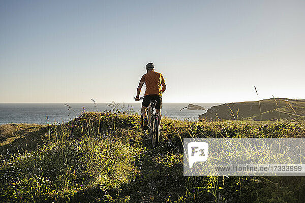 Männlicher Sportler  der bei Sonnenuntergang auf grünem Gras Rad fährt