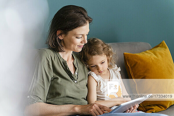 Mutter benutzt digitales Tablet  während sie mit ihrer Tochter zu Hause sitzt