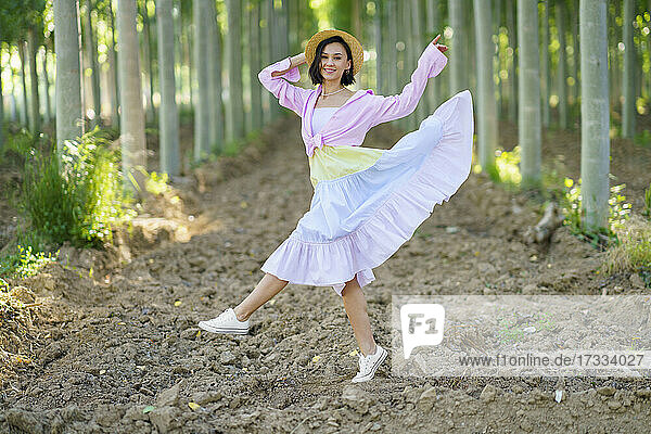 Lächelnde junge Frau mit Hut tanzt und genießt im Wald