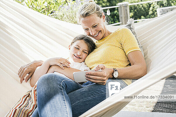 Mutter und Tochter lächelnd beim Entspannen in der Hängematte auf dem Balkon