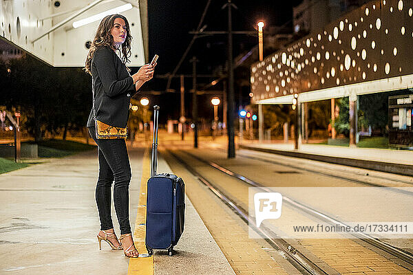 Female professional looking away while holding mobile phone at tram station