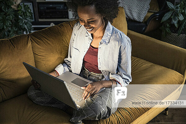 Lächelnde Geschäftsfrau  die einen Laptop benutzt und auf dem Sofa sitzt