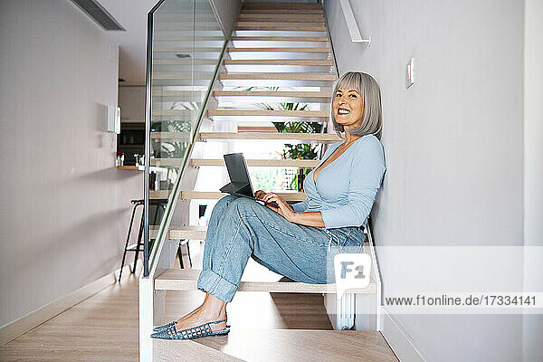Ältere Frau mit digitalem Tablet auf den Stufen zu Hause sitzend