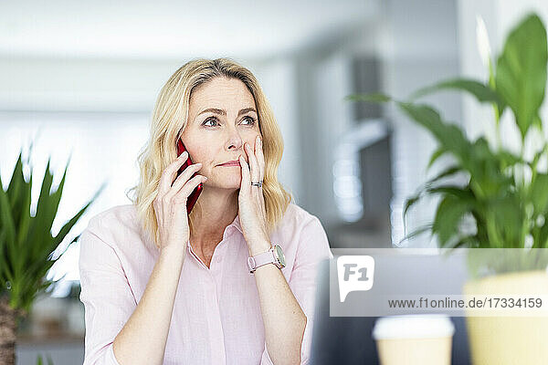 Nachdenkliche Geschäftsfrau  die im Büro zu Hause mit ihrem Smartphone telefoniert