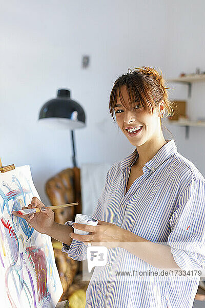Lächelnde Malerin hält Pinsel beim Malen im Atelier