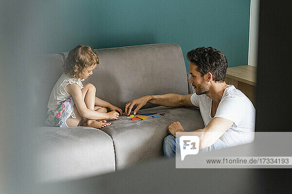 Vater hilft Tochter beim Spielen mit Puzzle auf Sofa