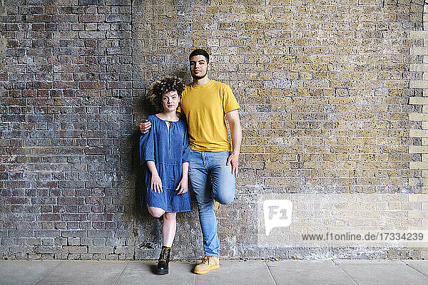 Young couple standing together on one leg in front of wall