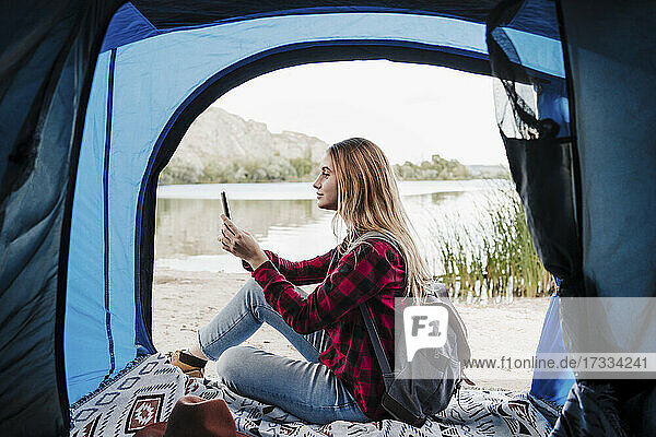 Junge blonde Frau  die im Zelt sitzend eine SMS über ihr Smartphone verschickt
