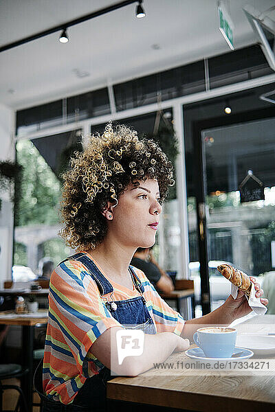 Frau isst Croissant  während sie am Tisch im Cafe sitzt
