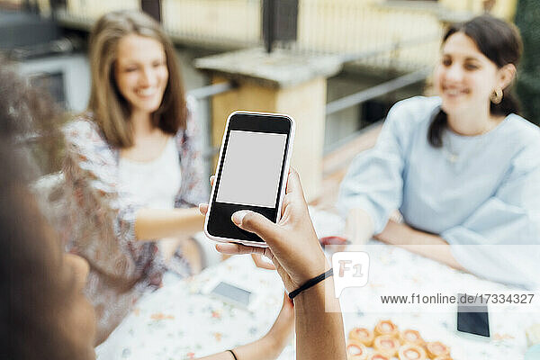 Woman using mobile phone while friends sitting at table in background