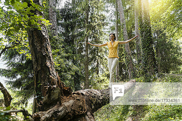 Woman with arms outstretched balancing while walking on tree in forest