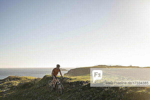 Male athlete cycling on grass near sea at sunset