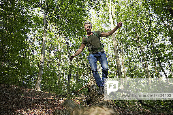 Man with arms outstretched walking on fallen tree in forest
