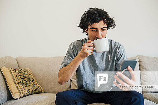 Man drinking coffee while using mobile phone at home
