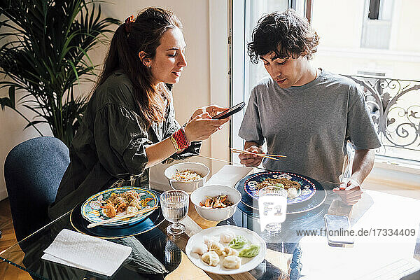 Freundin fotografiert Essen mit dem Mobiltelefon  während sie mit ihrem Freund zu Hause zu Mittag isst