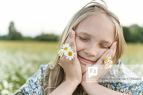 Blondes Mädchen mit Kamille Blumen lächelnd während Tag träumen im Feld