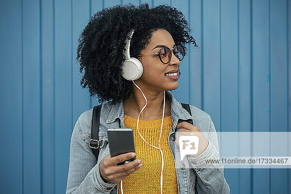 Frau schaut weg  während sie vor einer blauen Wand Musik über Kopfhörer hört