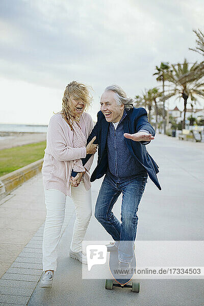 Älterer Mann genießt das Skateboardfahren mit einer Frau  die zu Fuß unterwegs ist und die Hände hält