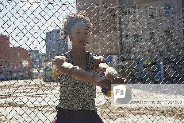 Female athlete exercising with kettlebell in front of chainlink fence