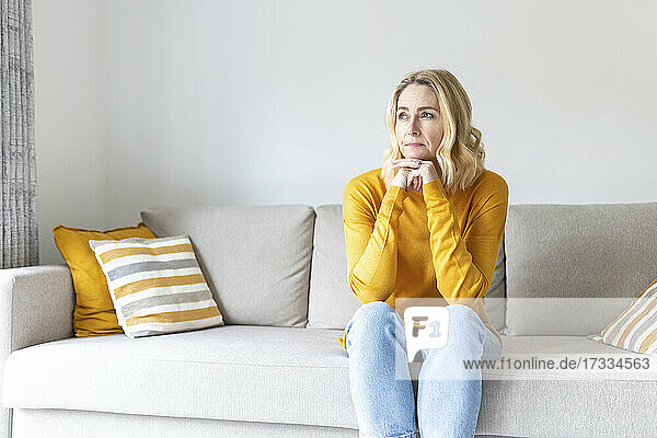 Thoughtful woman with hand on chin sitting on sofa at home