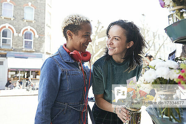 Lächelndes lesbisches Paar  das sich beim Kauf eines Blumenstraußes auf dem Markt gegenseitig anschaut