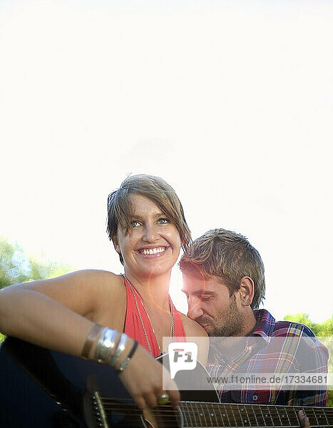 Man kissing shoulder of girlfriend playing guitar