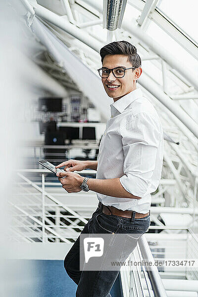 Smiling businessman holding digital tablet while leaning on railing