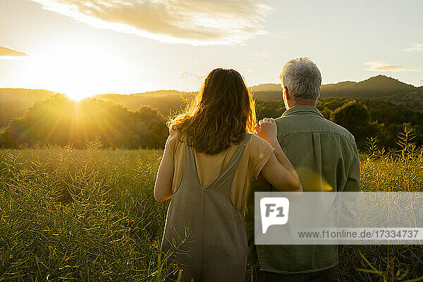 Tochter und Vater betrachten den Sonnenuntergang  während sie in einem Feld stehen