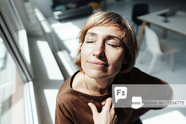 Geschäftsfrau mit geschlossenen Augen  stehend am Fenster im Büro
