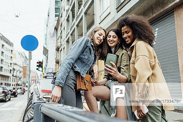Smiling friends taking selfie through smart phone in city