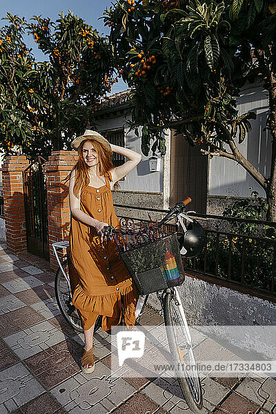 Lächelnde Frau auf dem Fahrrad sitzend auf dem Fußweg vor dem Haus