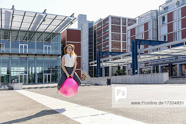 Junge Geschäftsfrau schaut weg  während sie an einem sonnigen Tag mit einem Hüpfball springt