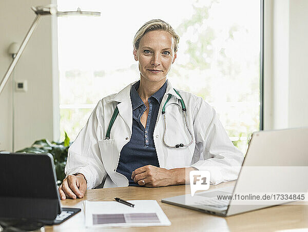 Ärztin mit Laptop und digitalem Tablet im Büro sitzend