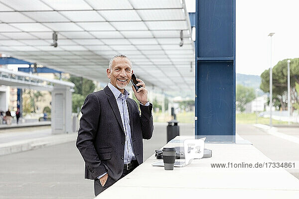 Geschäftsmann mit Laptop und Smartphone am Bahnhof