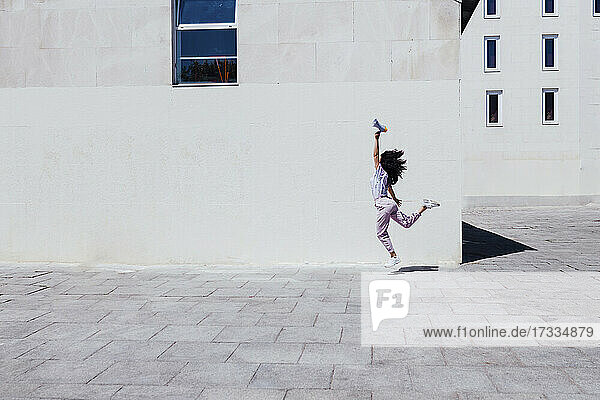 Young woman with hand raised holding megaphone while jumping by building during sunny day