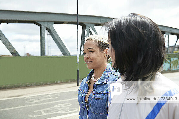 Lesbian woman looking at girlfriend while walking together on bridge