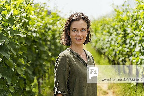 Smiling woman standing at vineyard during sunny day