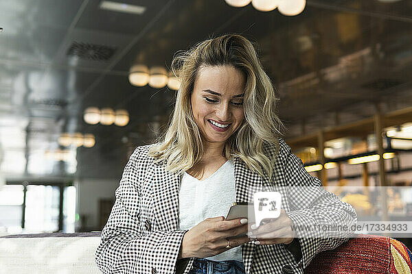 Smiling businesswoman with blond hair using smart phone at coffee shop