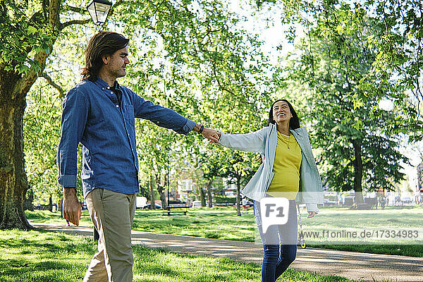 Smiling pregnant woman holding husband's hand while having fun in public park