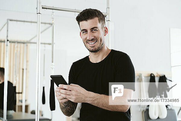 Lächelnder männlicher Besitzer mit Smartphone im Pilates-Studio