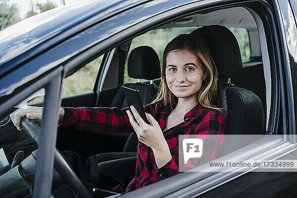Smiling beautiful woman holding smart phone sitting in car
