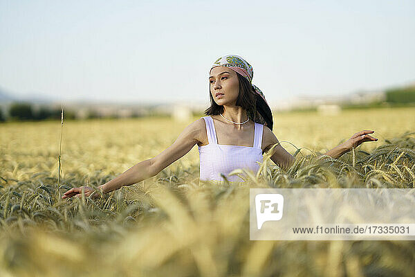 Junge schöne Frau mit Kopftuch steht in einem Weizenfeld und schaut weg