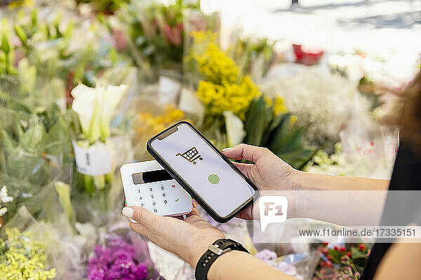 Woman holding smart phone while doing contactless payment at flower shop