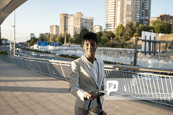 Businesswoman with electric scooter standing on footbridge in city