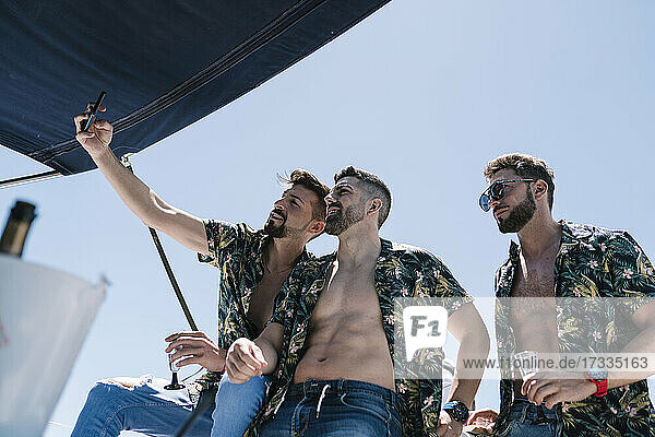 Mann nimmt Selfie durch Handy mit männlichen Freunden während Party auf Yacht