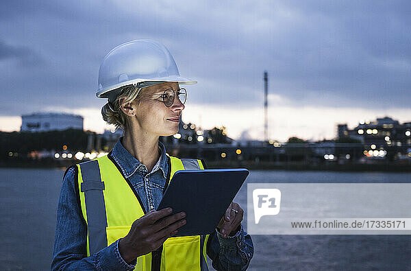 Weiblicher Arbeiter  der wegschaut  während er ein digitales Tablet bei Nacht hält