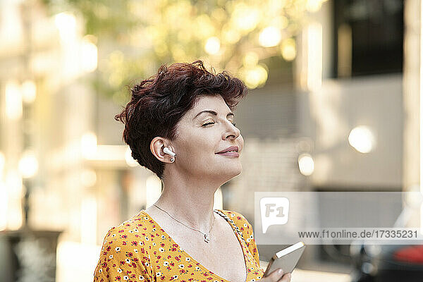 Lächelnde reife Frau mit geschlossenen Augen  die Musik über In-Ear-Kopfhörer hört