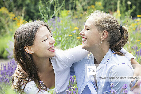 Female friends with arms around having fun amidst flowering plants